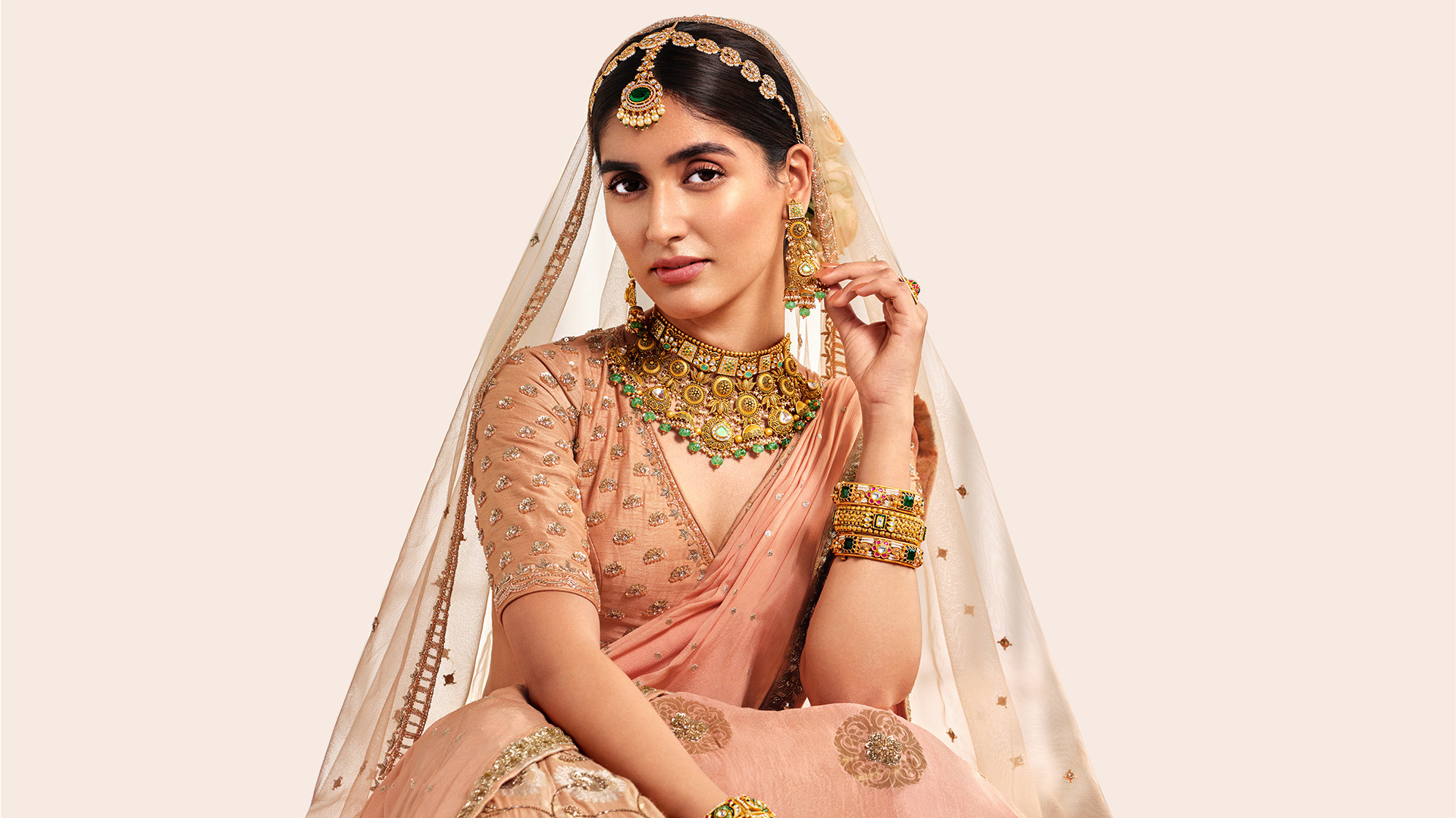 Indian woman in a pink lehenga with antique gold kundan jewelry, including gold bangles, a statement necklace with green stones, and gold rings.